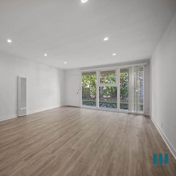 a spacious room with wooden flooring and a sliding glass door leading to a balcony.