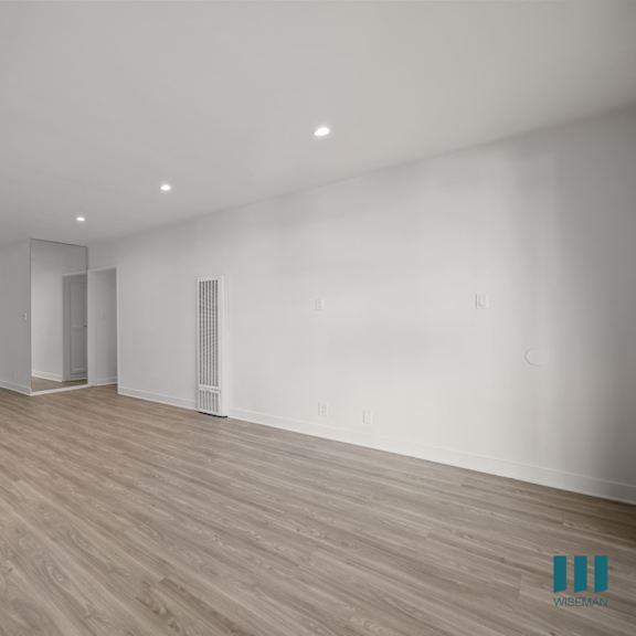 a spacious room with wooden flooring and white walls.