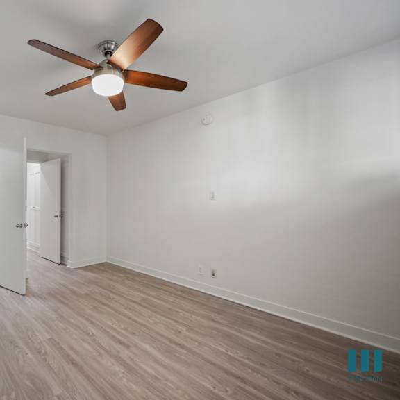 a room with a ceiling fan and light, wooden floors, and white walls.