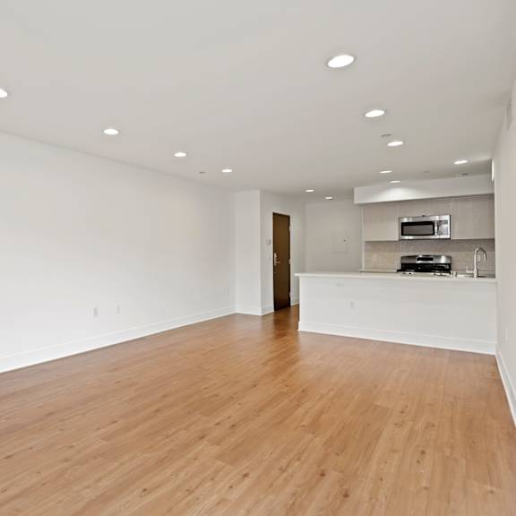 an empty living room with a kitchen in the background