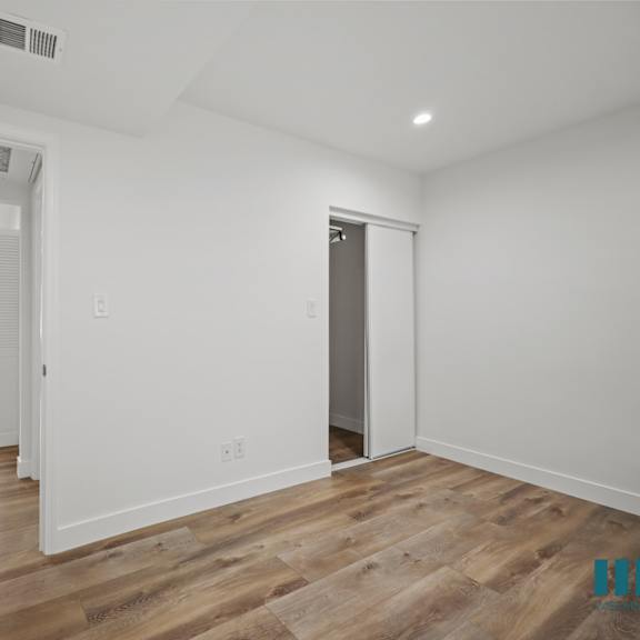 a room with white walls and wooden flooring, with a door on the left and a window on the right.