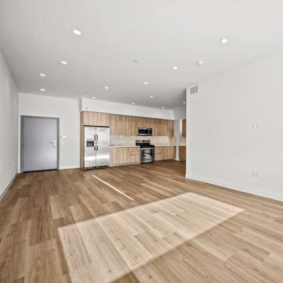 a spacious room with wooden flooring and a kitchen area in the background.