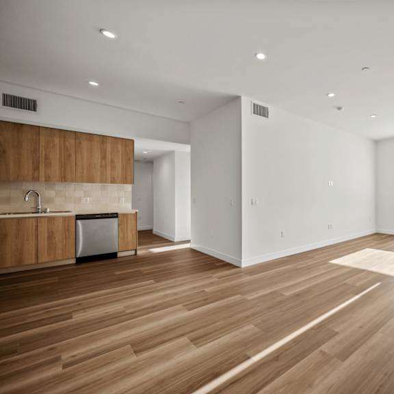 a spacious room with wooden flooring and a kitchen area with white walls.