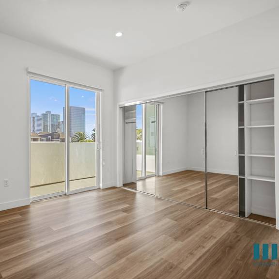 a spacious room with wooden flooring and a view of the city through a large window.