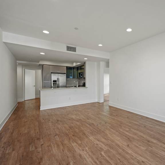 a large empty room with wooden floors and a kitchen area in the background.