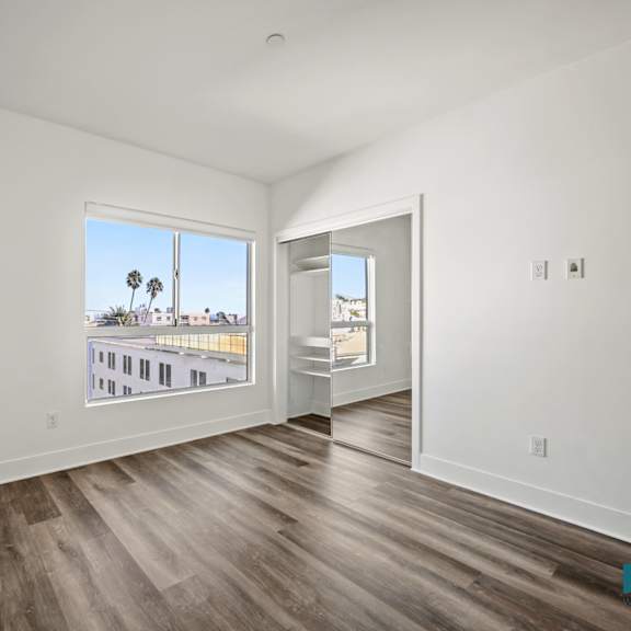 a room with wooden floors and a view of a street with palm trees.
