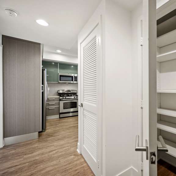 a white door is open to a hallway with a kitchen in the background.