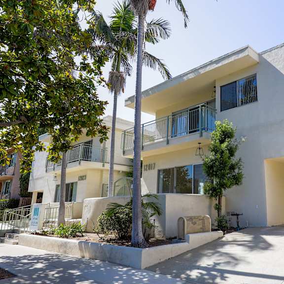 the exterior of a yellow and white building with palm trees