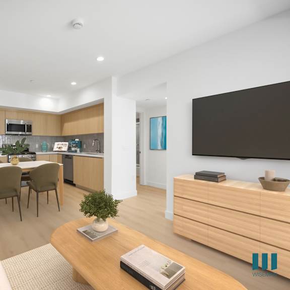 a modern living room with a white sofa, wooden coffee table, and a kitchen area in the background.