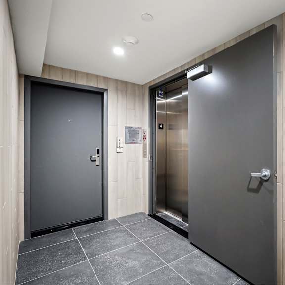 a hallway with a grey elevator and a black door on the left.