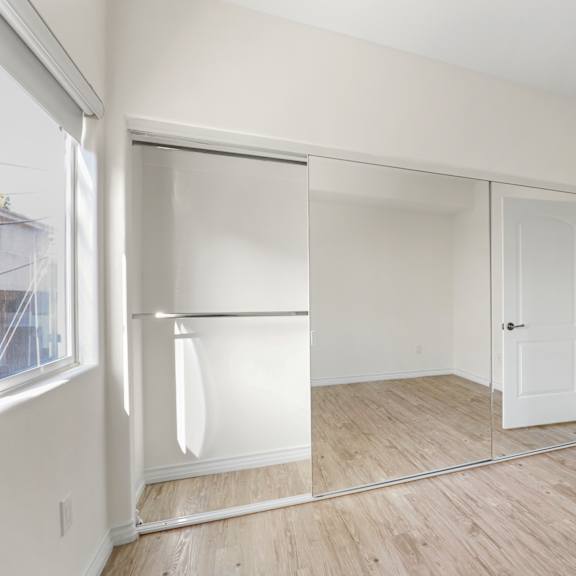 large bedroom with full-size mirrored closet, vinyl flooring, and window