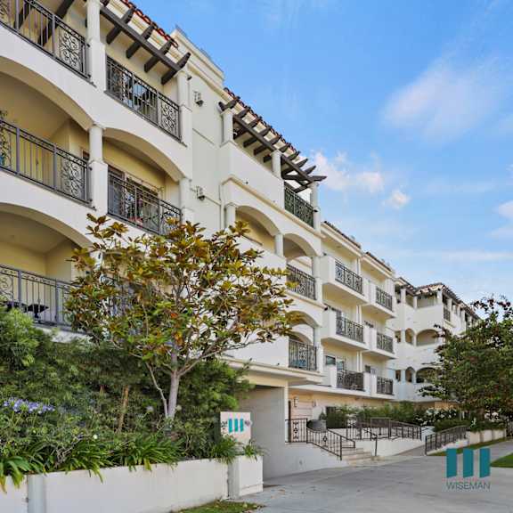 a large white apartment building with trees and a sidewalk