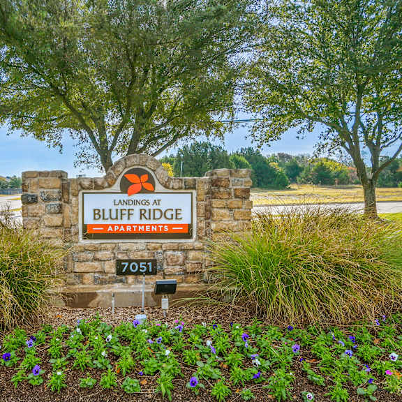 a sign for bluff ridge apartments is surrounded by flowers and greenery.