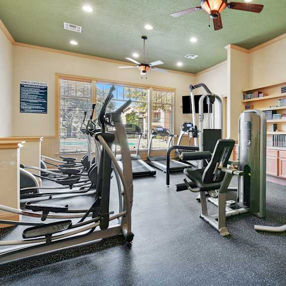 a gym with treadmills, weights, and a fan.