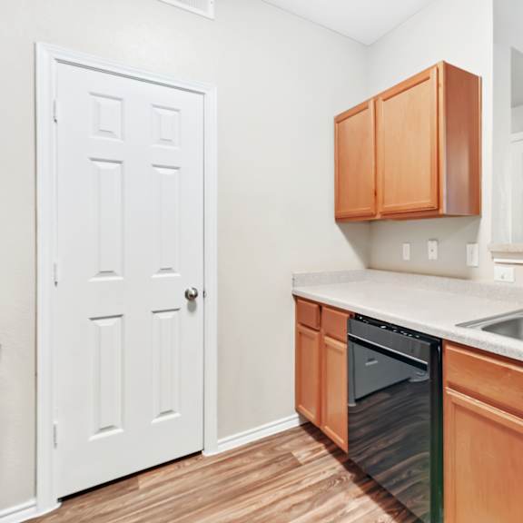 a kitchen with a white door, brown cabinets, and a black dishwasher.