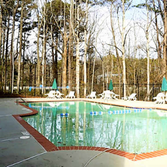 a pool surrounded by trees and chairs at clarkston station apartments, clarkston, georgia