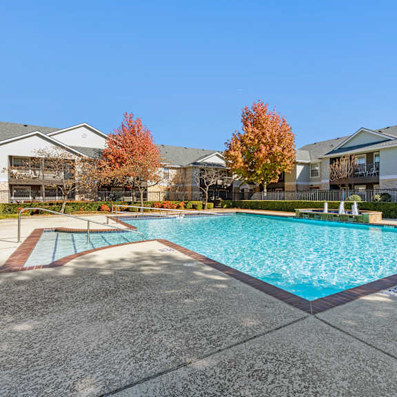 a swimming pool surrounded by a concrete floor and residential buildings.