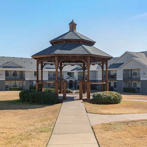 a gazebo is in the middle of a grassy area in front of apartment buildings.