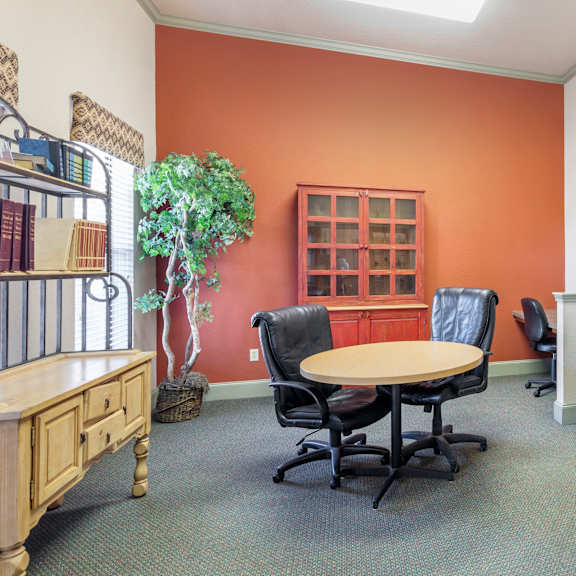 a room with orange walls has a table, chairs, and a bookcase.