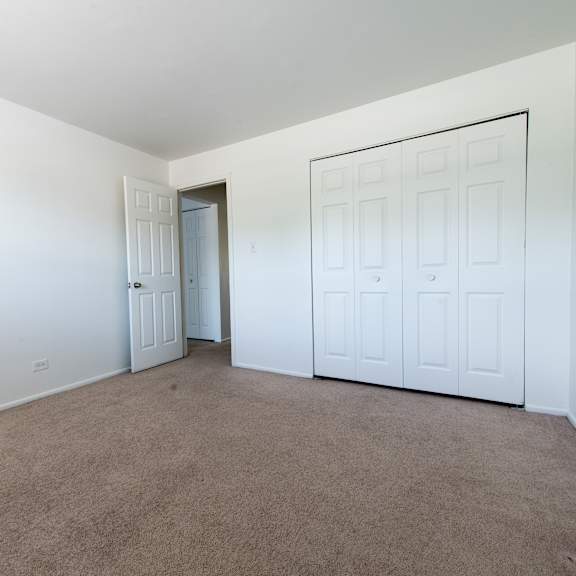 a bedroom with white walls and carpet and a door to a closet