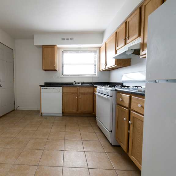 an empty kitchen with white appliances and wooden cabinets
