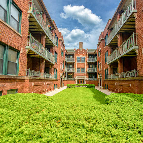 a green lawn in front of a brick building with balconies.