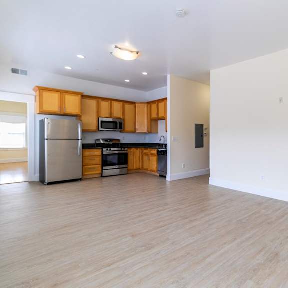 a kitchen with wooden cabinets, a refrigerator, and living room.
