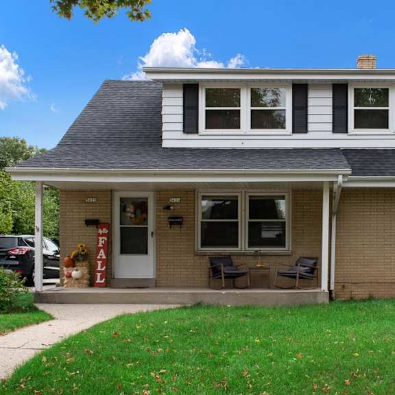 a brick house with a gray roof and a green lawn with a blue sky in the background