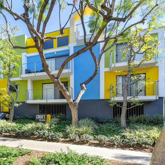 blue/yellow/green apartment exterior with view of private patio, trees, bushes at croft plaza apartments, west hollywood, 90069