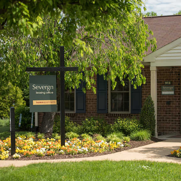 exterior view of a brick leasing office with windows, beautiful trees and colorful flowers at severgn apartments in exton, pa.