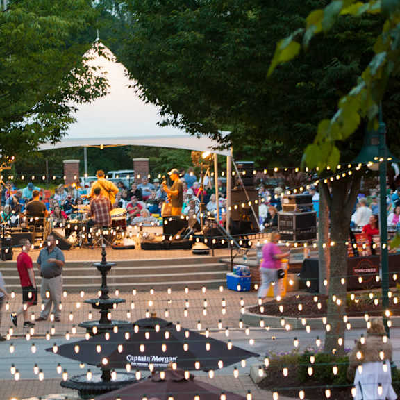 an outdoor stage with musician performing for a crowd near hanging string lights and trees at an eagleview concert in exton, pa.
