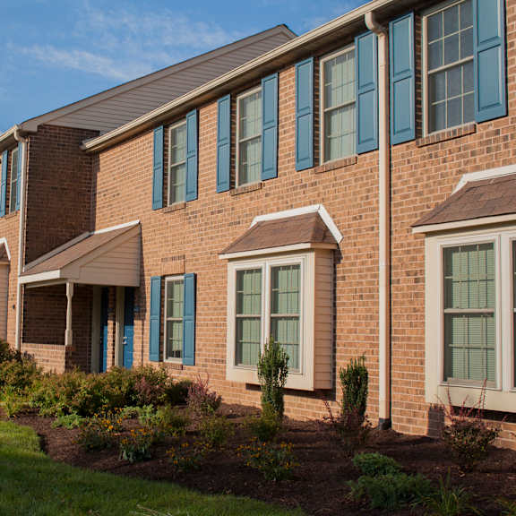 an exterior view of our severgn's two-story brick apartment buildings with beautiful landscaping lining a sidewalk.