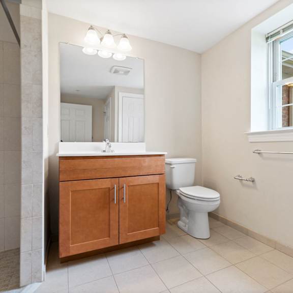 a large bathroom with full-size vanity, a window, overhead mirror lighting, tile flooring, and a stand-up shower.