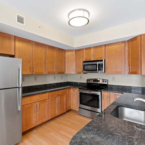 a u-shaped kitchen with stainless steel appliances, granite countertops, modern wooden cabinets, and hardwood-style flooring.
