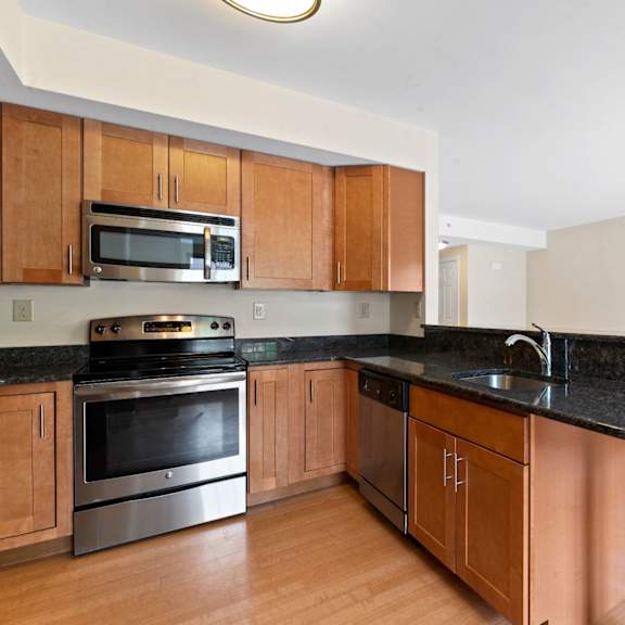 a kitchen with hardwood-style floors, black granite countertops, beautifully-designed breakfast bar, and stainless steel appliances.