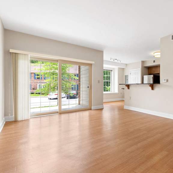 a spacious living room with hardwood style flooring and large sliding glass doors to a private patio near a dining area and kitchen.