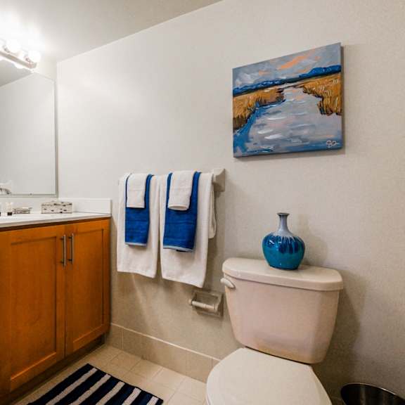 a bathroom with a full-sized mirror, spacious vanity with under-cabinet storage space, a towel bar, tile flooring, and a toilet.