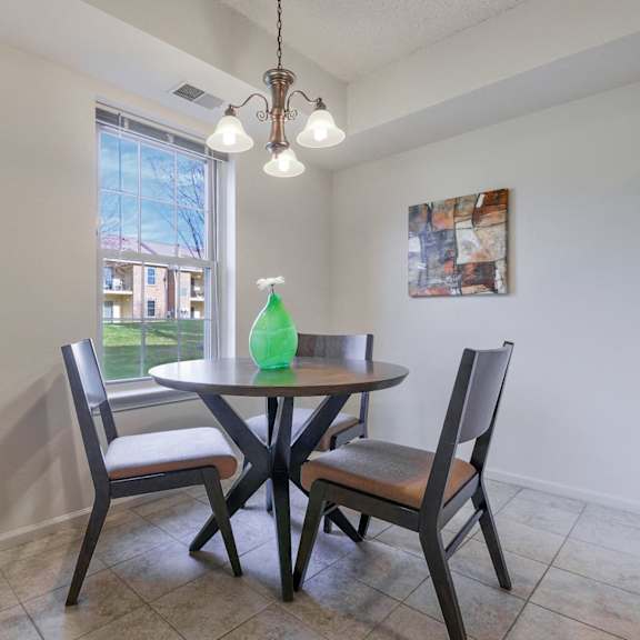 a quaint dining room with a window, hanging chandelier, and tile flooring near a kitchen.
