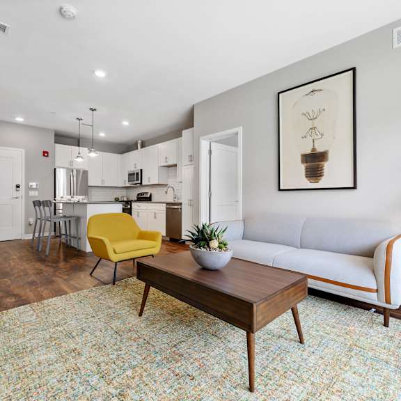 a living room with hardwood-style flooring, natural light, high ceilings, and open access to the kitchen with a breakfast bar.