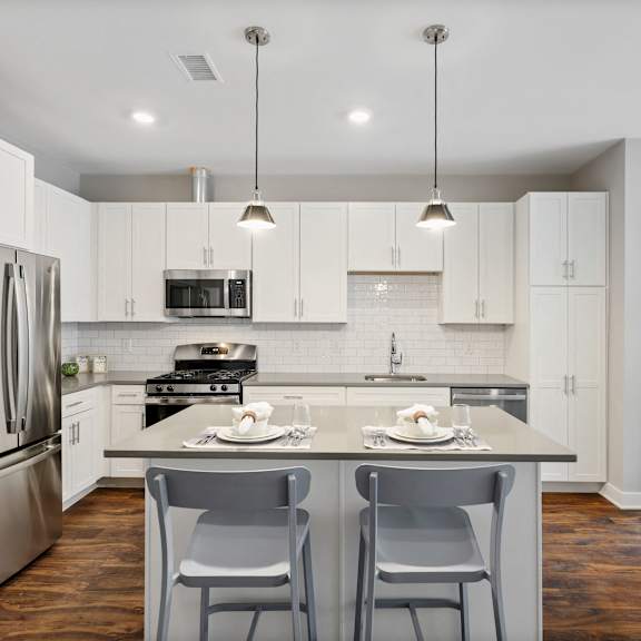 a large l-shaped kitchen with pendant and recessed lighting, hardwood-style flooring, stainless steel appliances, and kitchen island near a bedroom.