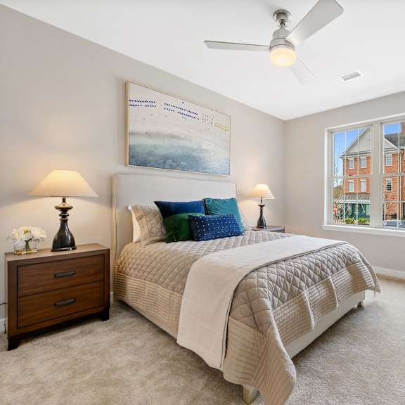 a bedroom with a large window, ceiling fan, and carpet flooring.