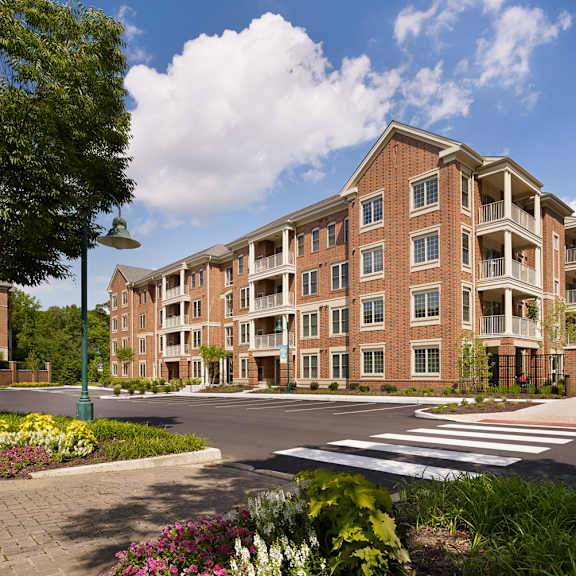 exterior view of claremont on the square 4-story apartment buildings in exton, pa with nearby resident parking and beautiful trees and flowers.