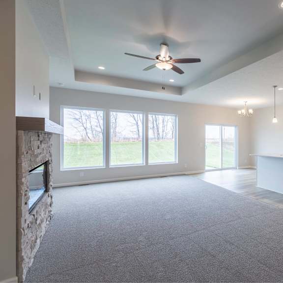 a spacious living room with a ceiling fan and a kitchen area in the background.