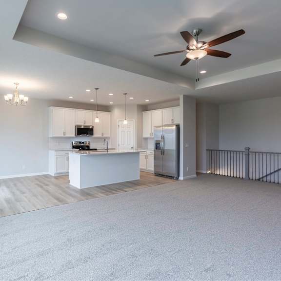 a spacious, empty room with a ceiling fan and a kitchen area in the background.