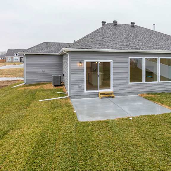 a grey house with a concrete patio and a white fence.