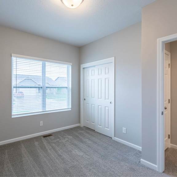 a room with a carpeted floor, a window with blinds, and a white door.