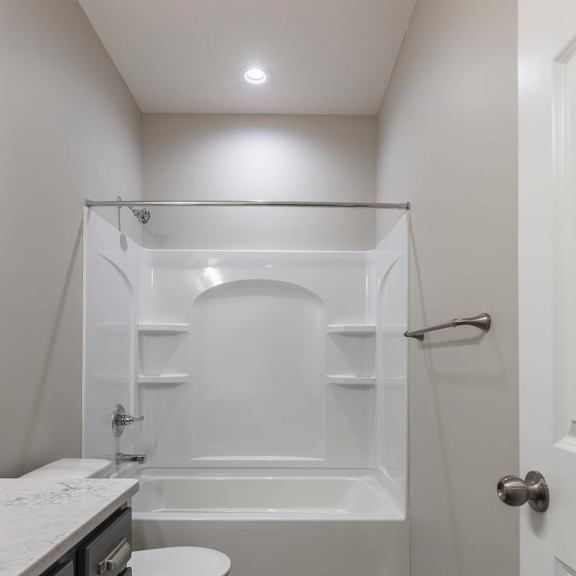 a white toilet sits in a small bathroom with a walk-in shower.