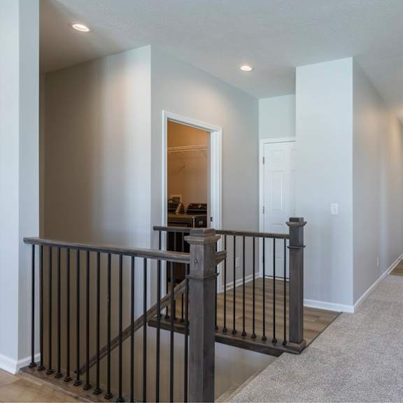 a hallway with a black railing and white walls.