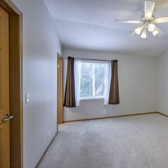 a room with a ceiling fan and a window with curtains.
