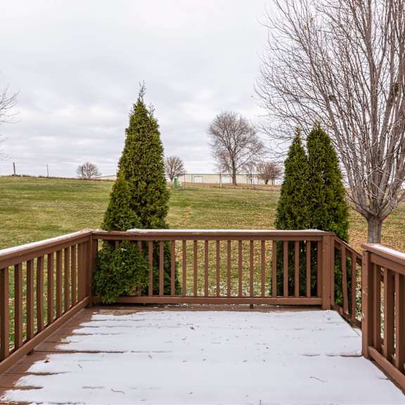 a wooden deck with snow on it and evergreen trees in the background.